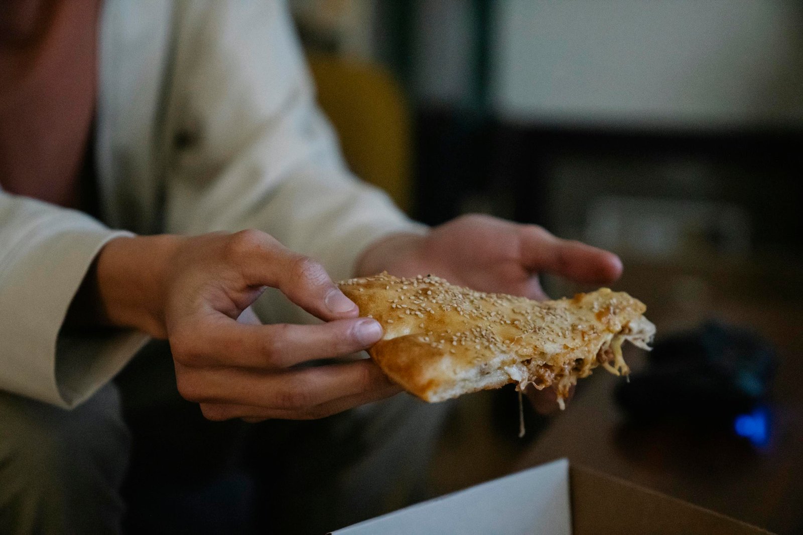 Crop unrecognizable male with tasty pie piece with sesame seeds on top in house room